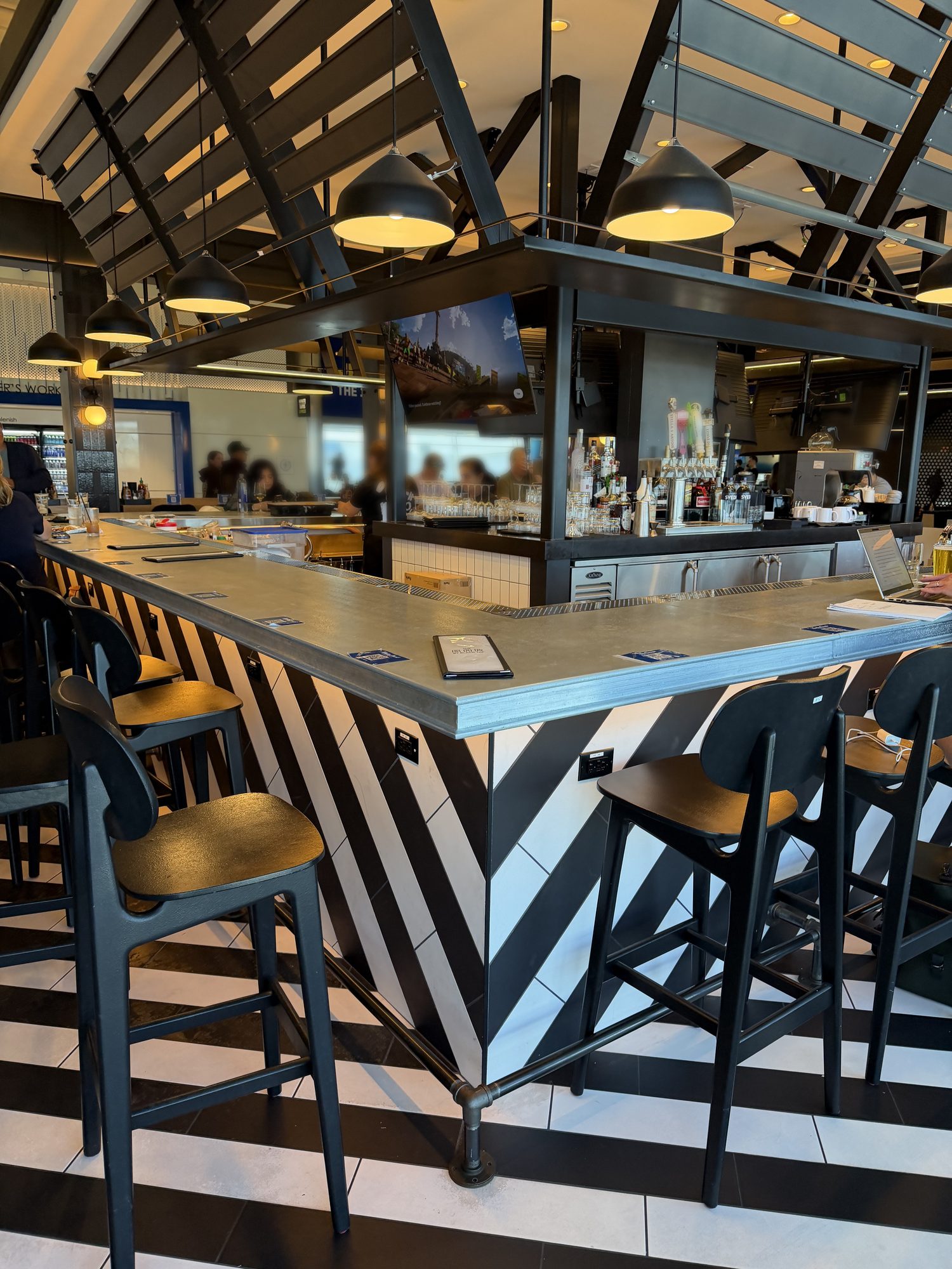 Zinc bar top with a profiled edge over black-and-white chevron tile at The Bar by Black Tap, JFK Terminal 8, New York