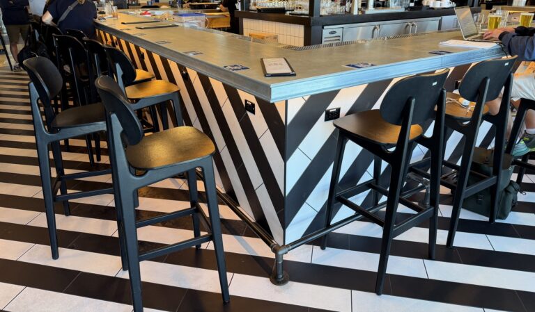 Zinc bar top lined with black bar stools at The Bar by Black Tap, JFK Terminal 8