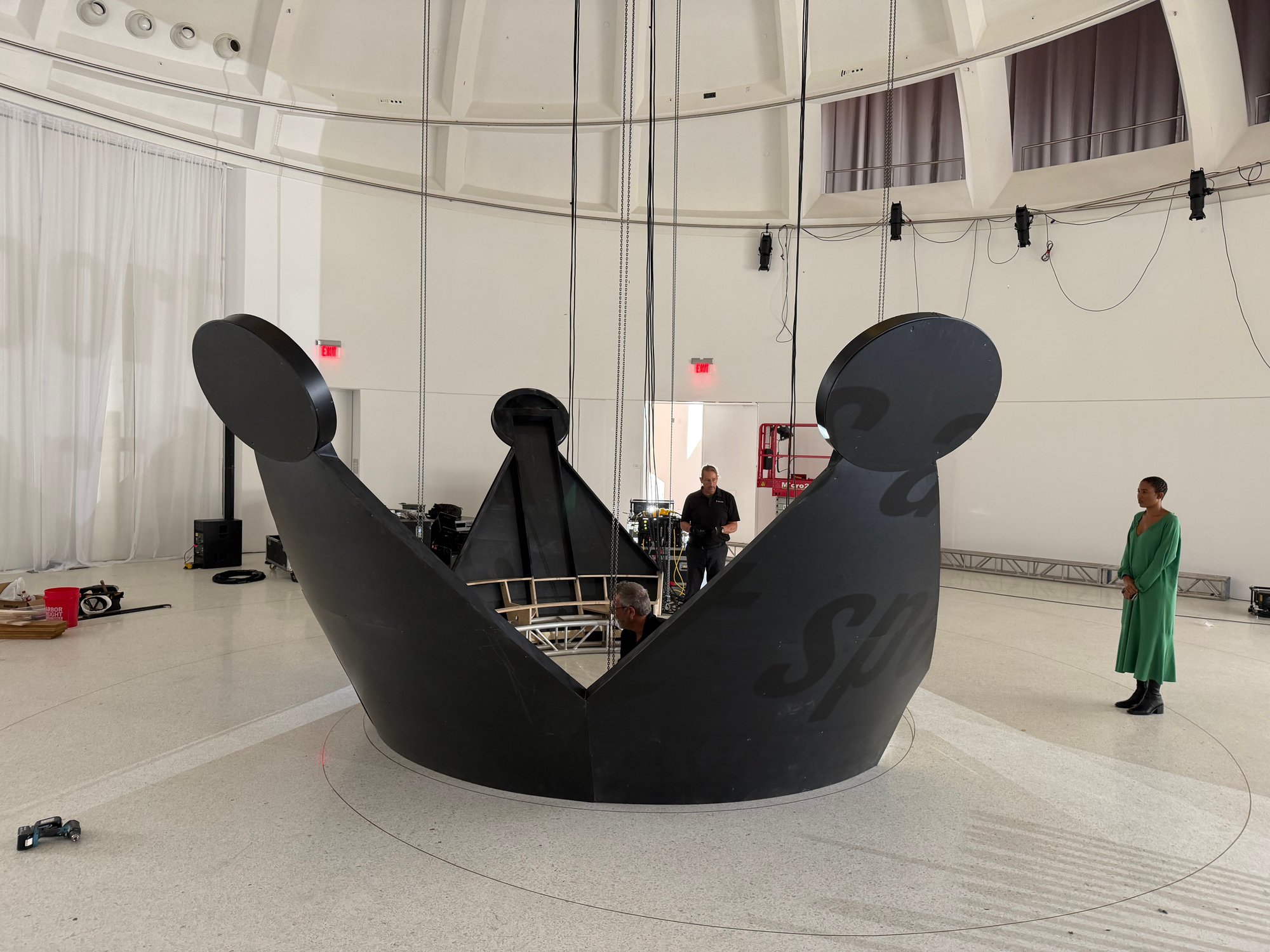 Crew working inside the matte-black crown assembled on the floor under the dome at Faena Miami Beach, with a woman standing beside it