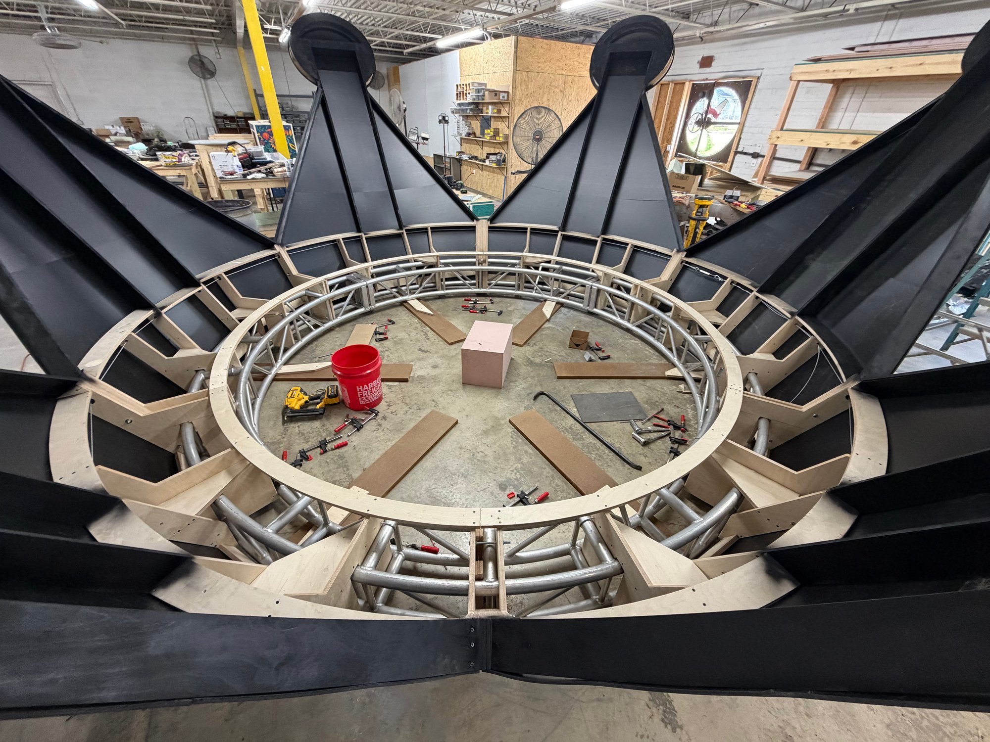 Overhead view of the crown assembled on the shop floor, matte-black points around a circular aluminum truss ring and plywood framing, for Faena Miami Beach