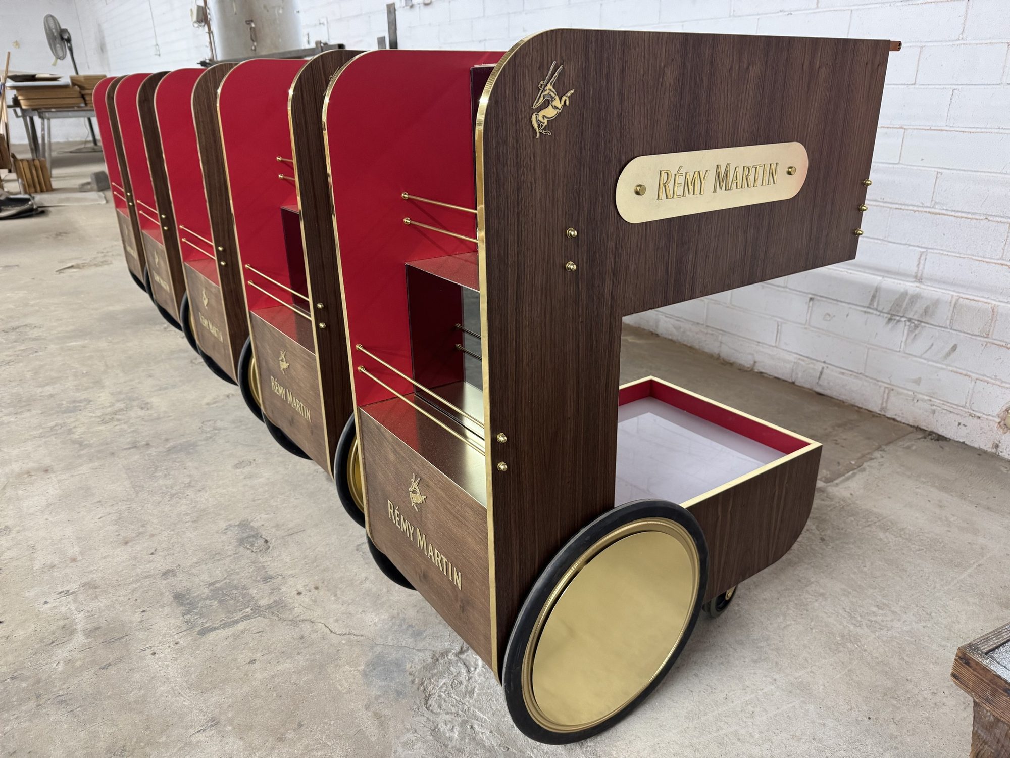 Row of custom Rémy Martin bar carts with brass-toned wheel covers and walnut-look shells